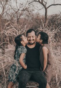 A father sits between his 2 daughters as they kiss him on each cheek.